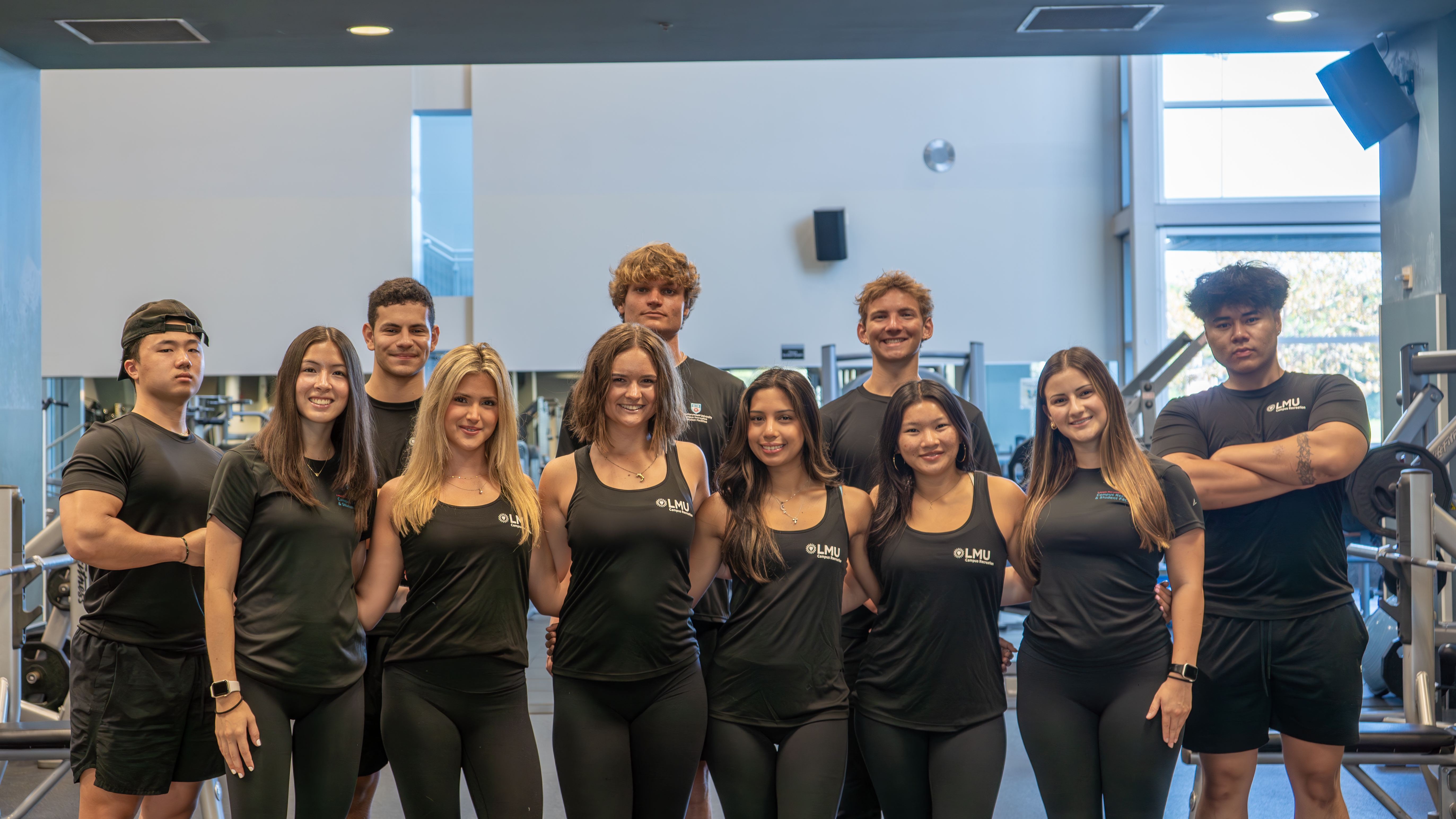 A group shot of student personal trainers in the weight room wearing all black.